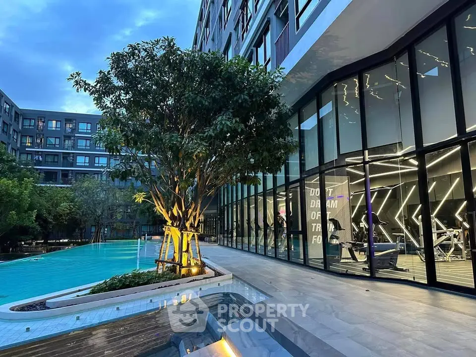Luxurious modern apartment complex with pool and gym facilities at dusk.