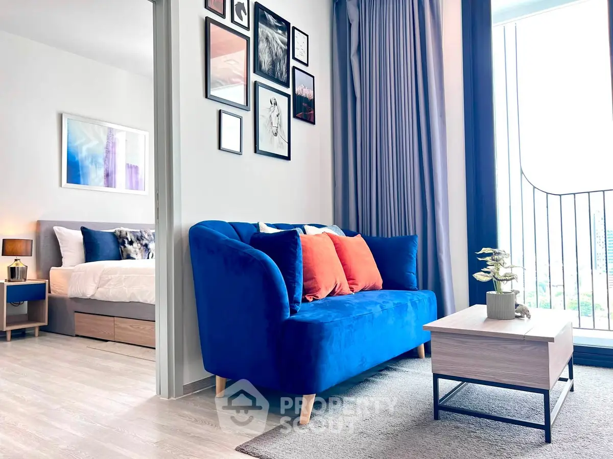Modern living room with blue sofa and bedroom view, featuring stylish decor and natural light.