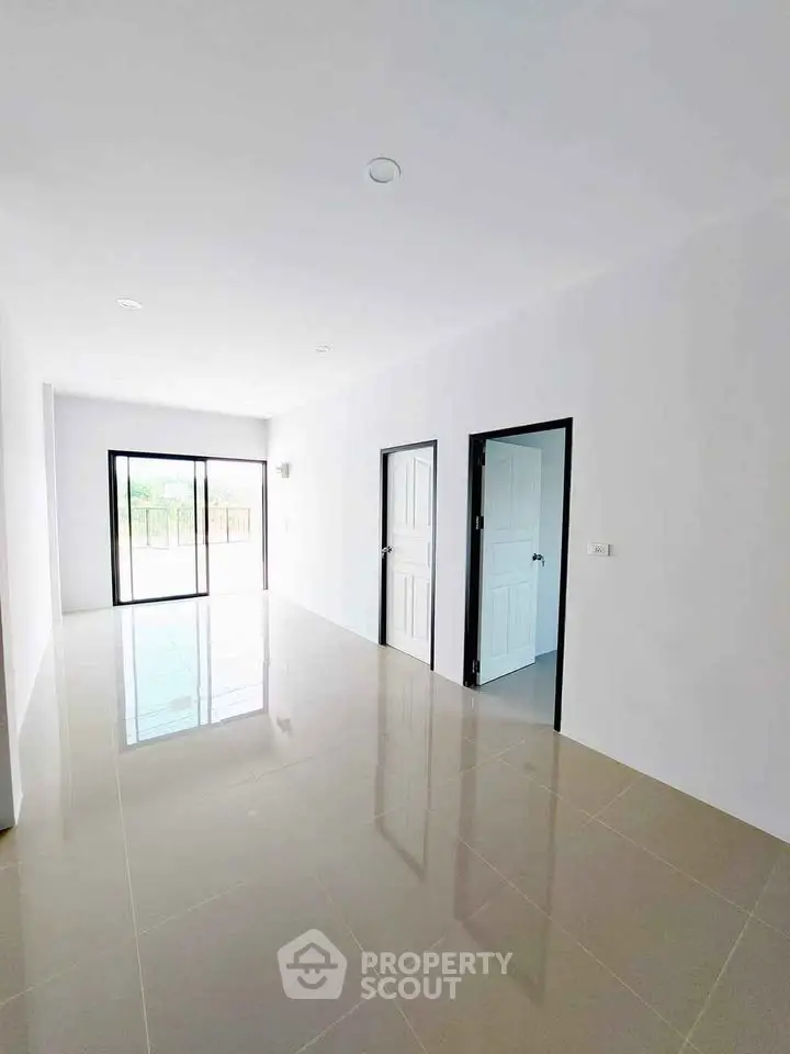 Spacious empty room with glossy tiled floor and sliding glass doors leading to a bright outdoor area.