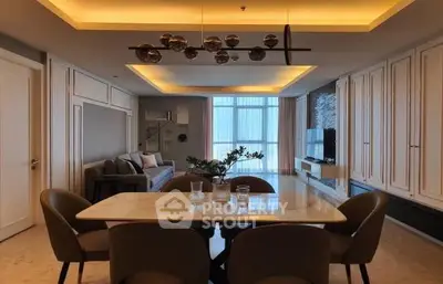 Elegant dining area seamlessly connects to a modern kitchen, featuring chic lighting, ample cabinetry, and a cozy living space in the background.