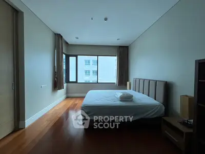 Spacious bedroom with large window and wooden flooring in modern apartment