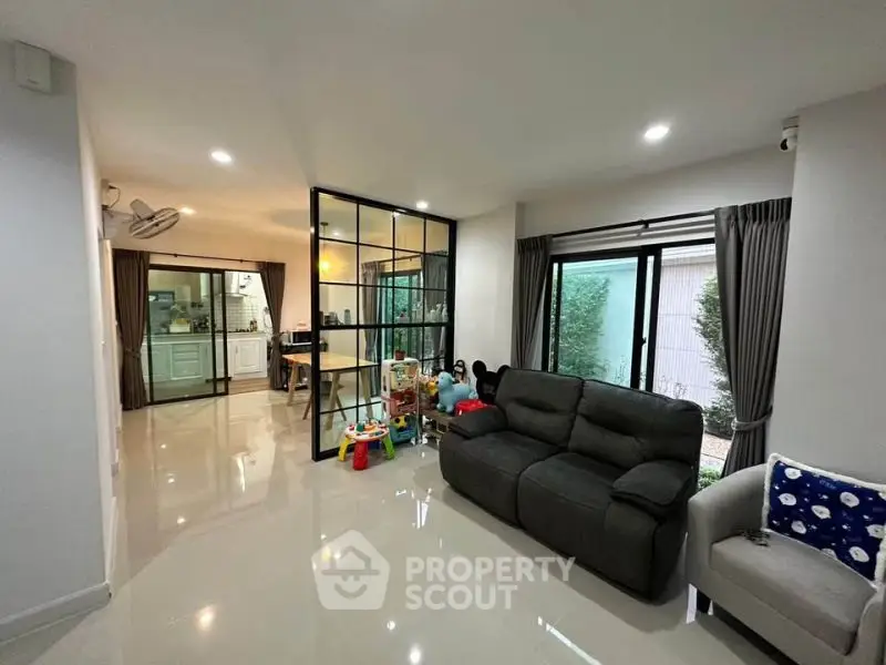 Modern living room with sleek design and open kitchen layout, featuring large windows and stylish furniture.