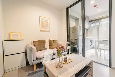 Modern living room with cozy sofa and stylish decor, adjacent to a sleek kitchen with glass partition.