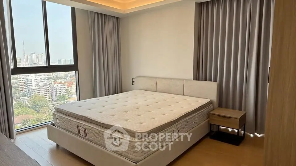 Spacious bedroom with city view and modern furnishings in a high-rise apartment.
