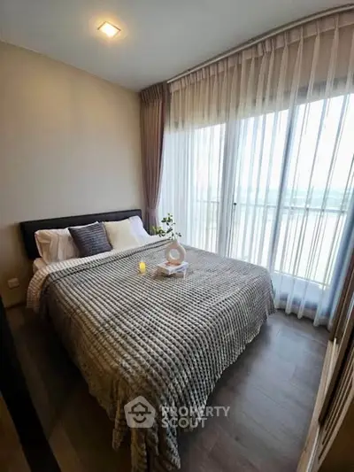 Cozy bedroom with large window and elegant curtains, featuring a comfortable bed and stylish decor.