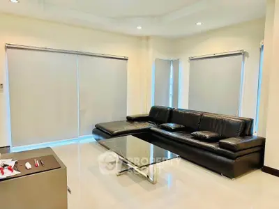 Modern living room with sleek black leather sofa and glass coffee table, featuring large windows with blinds.