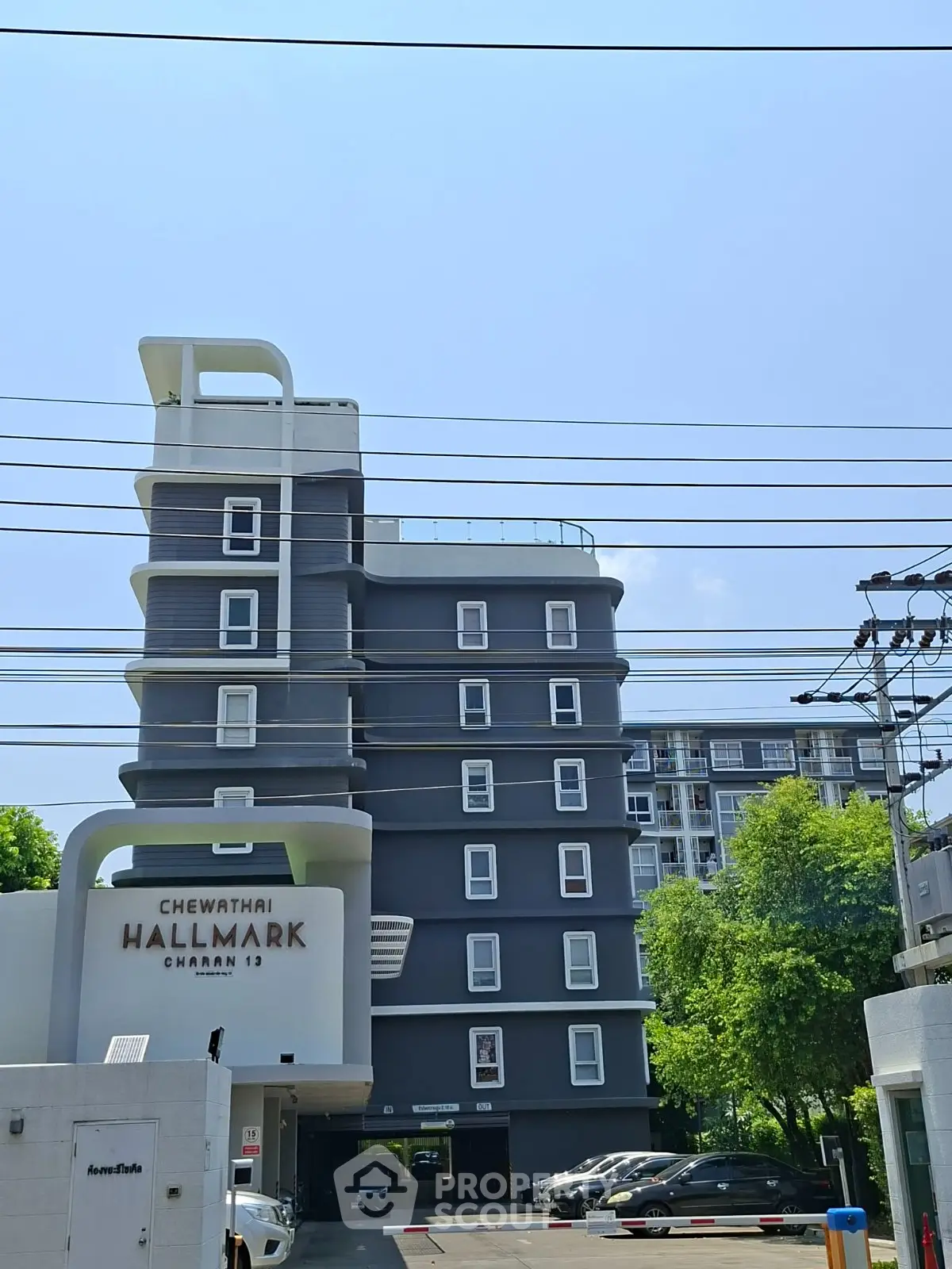 Modern apartment building exterior with parking area and lush greenery, ideal urban living space.