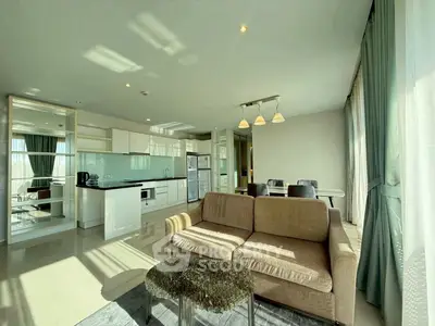 Spacious modern living room with open kitchen and dining area, featuring large windows and elegant furnishings.