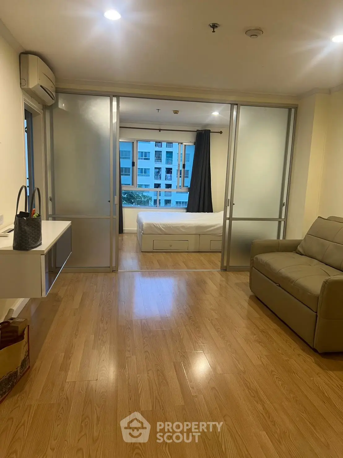 Spacious modern living room with sliding doors leading to a cozy bedroom, featuring wooden flooring and natural light.