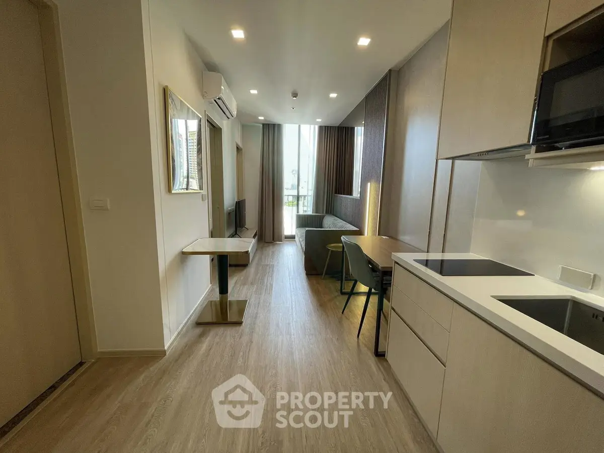 Modern open-layout apartment with sleek kitchen and cozy living area, featuring elegant wooden flooring and ample natural light.