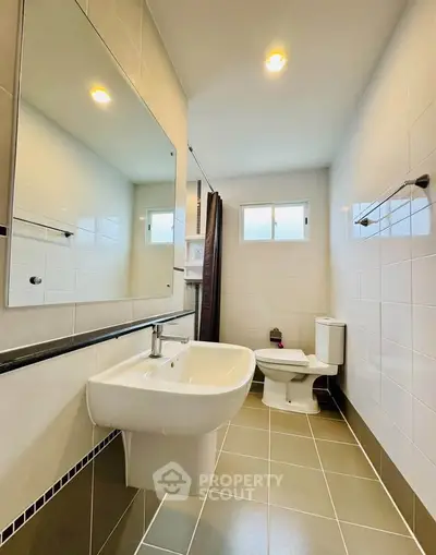 Modern bathroom with sleek fixtures and neutral tiles, featuring a large mirror and natural light.
