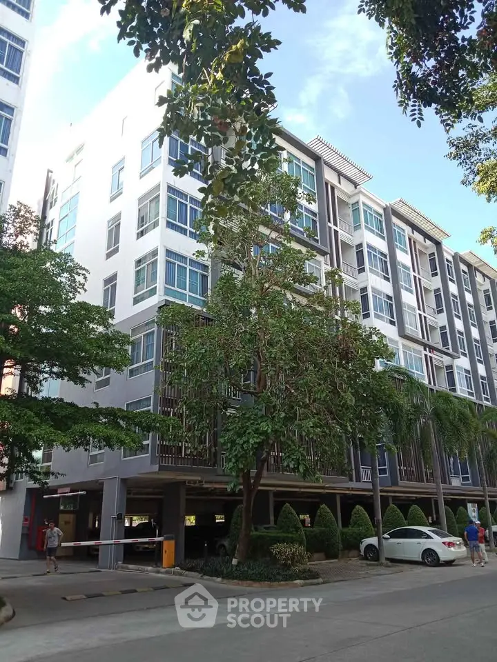 Modern apartment building with lush greenery and ample parking space in a serene neighborhood.