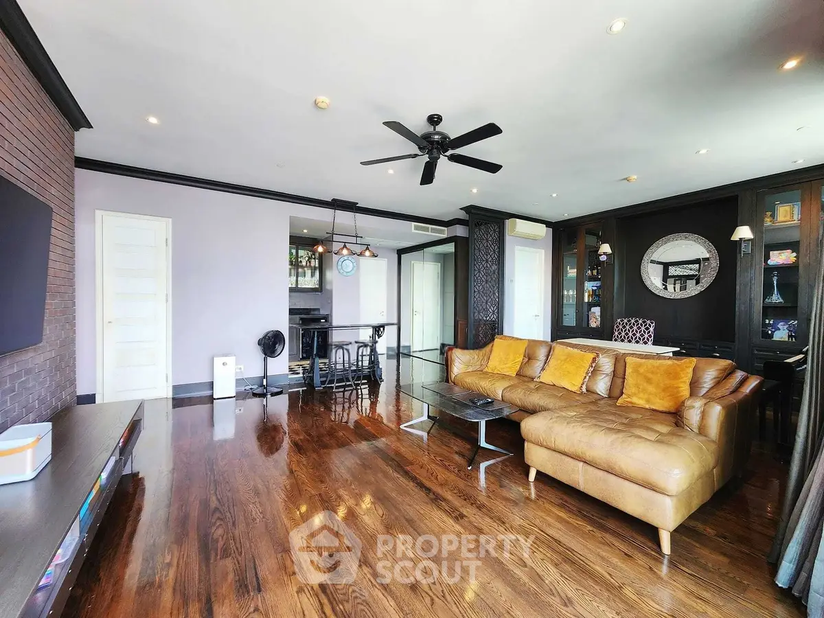 Spacious living room with elegant decor and hardwood floors, featuring a stylish leather sofa and modern ceiling fan.