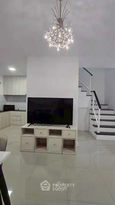 Modern living room with elegant chandelier and sleek staircase, featuring a large TV and stylish open layout.