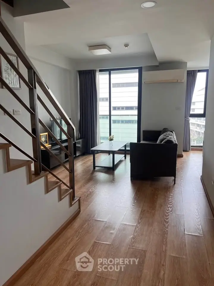 Modern living room with wooden flooring and large windows offering city views.