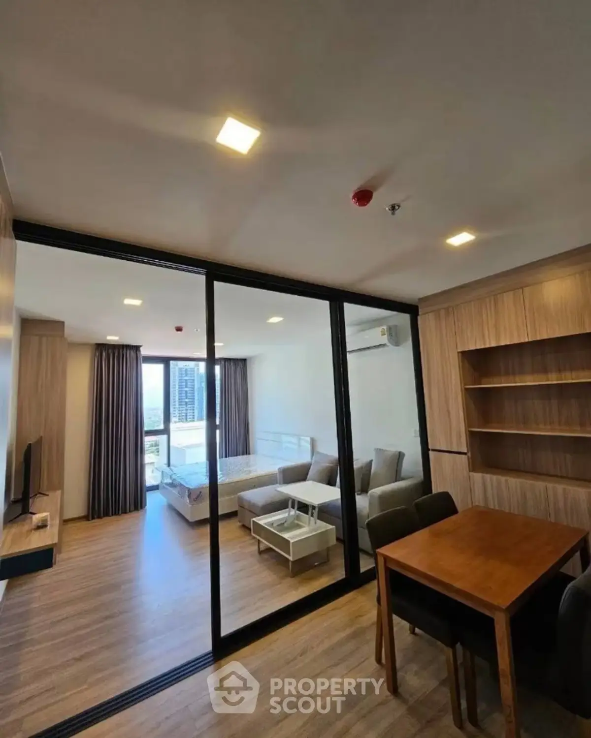 Modern open-plan living room with glass partition and city view, featuring stylish furniture and wooden flooring.