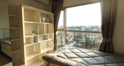 Bright bedroom with large window and city view, featuring modern shelving and cozy bedding.
