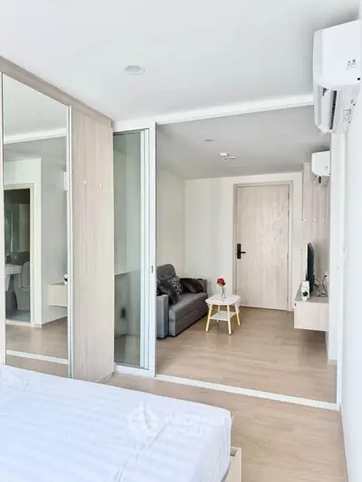 Modern bedroom with mirrored closet doors and cozy living area in a stylish apartment.