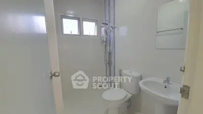 Modern bathroom with shower, toilet, and sink in bright white tiles.