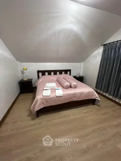Cozy attic bedroom with sloped ceiling and wooden flooring, featuring a neatly made bed and bedside tables.