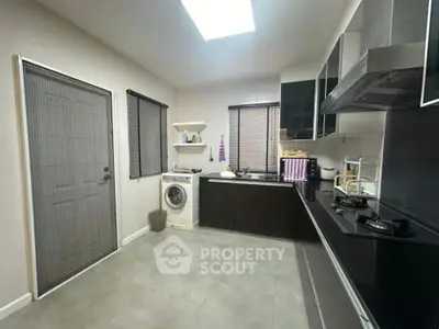 Modern kitchen with sleek black cabinets and gas stove, featuring a washing machine and ample natural light.