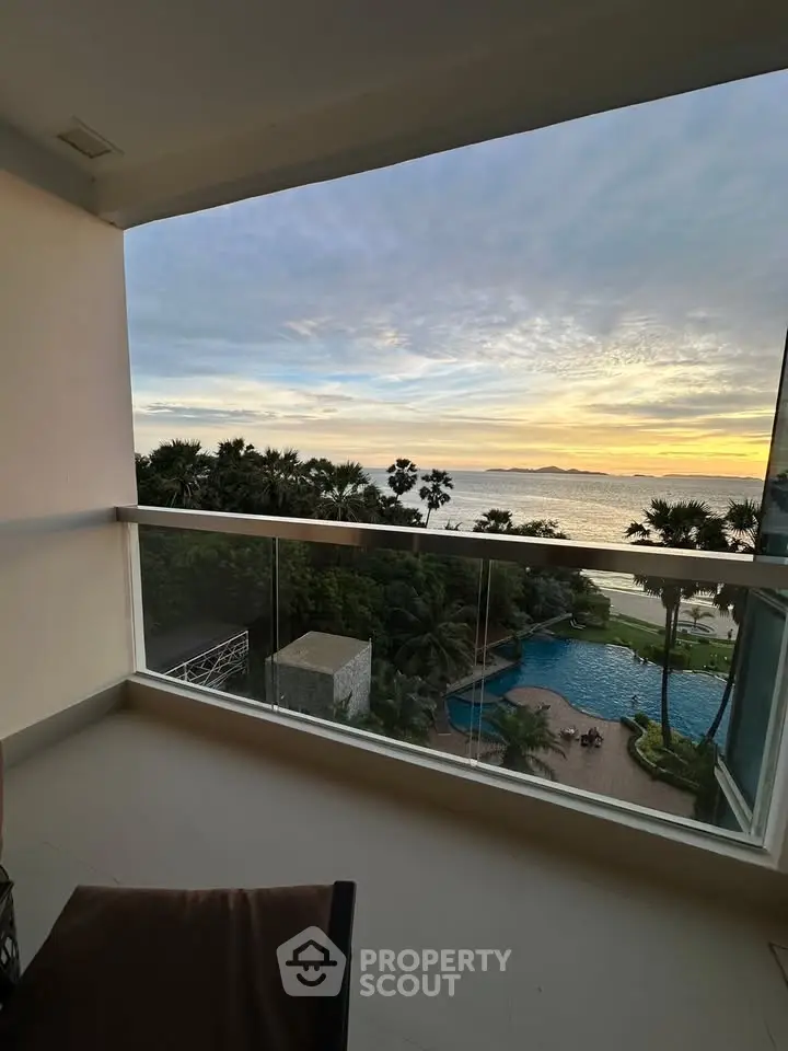 Stunning ocean view from a spacious balcony overlooking a pool and lush greenery at sunset.