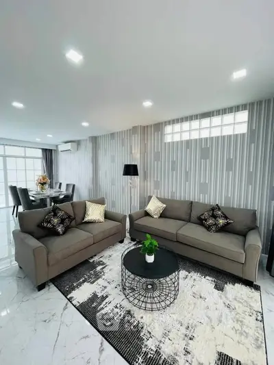 Modern living room with stylish decor and elegant dining area, featuring sleek sofas and contemporary lighting.
