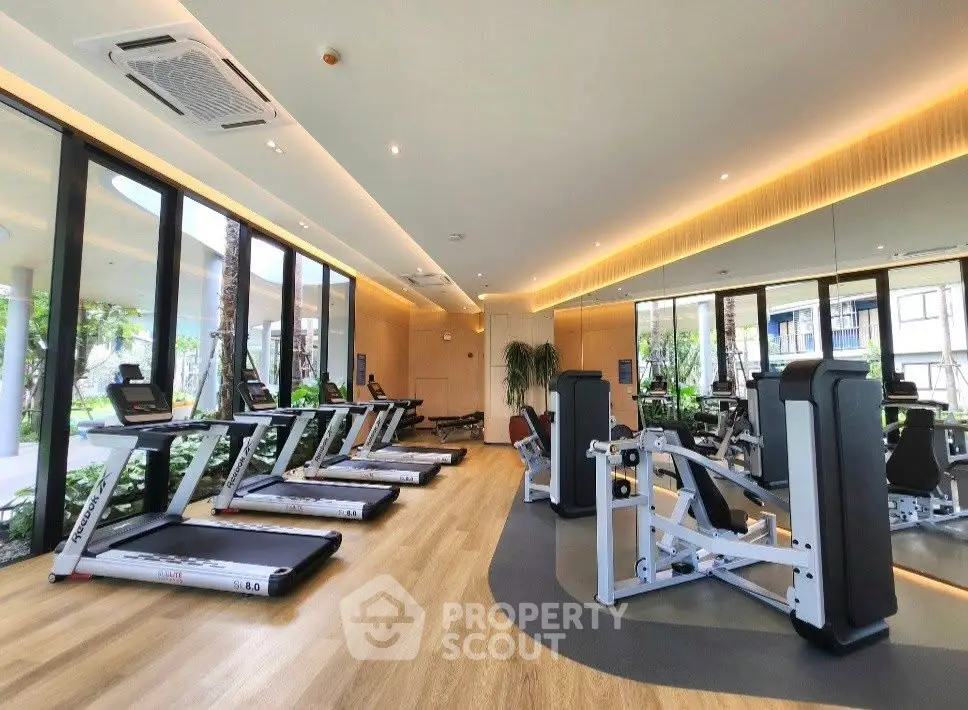 Luxurious gym with modern equipment and floor-to-ceiling windows in upscale residential building.
