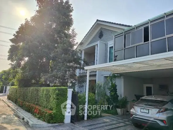 Charming suburban house with lush garden and spacious carport under sunny sky.