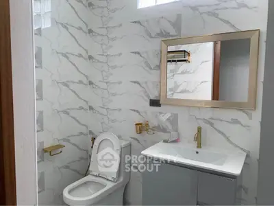 Luxurious bathroom with marble walls and modern fixtures, featuring a sleek vanity and elegant mirror.