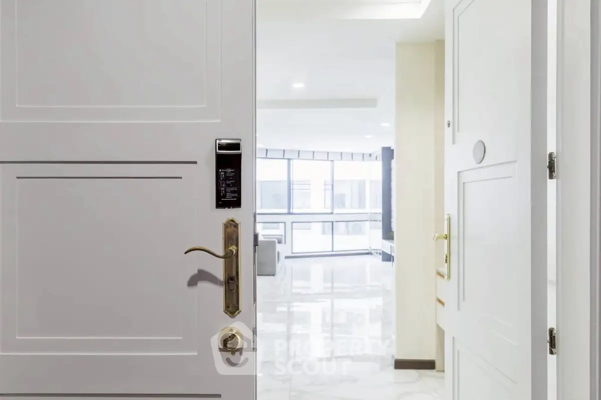 Modern apartment entrance with open door revealing bright living space and large windows.