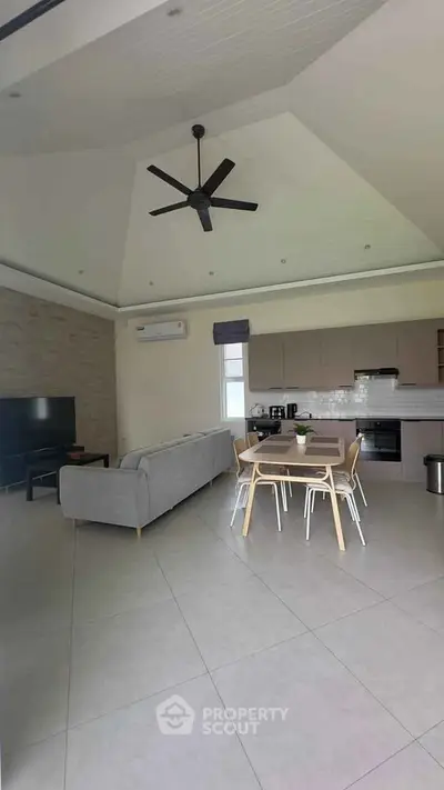 Modern open-plan living room with sleek kitchen and dining area, featuring a ceiling fan and stylish decor.