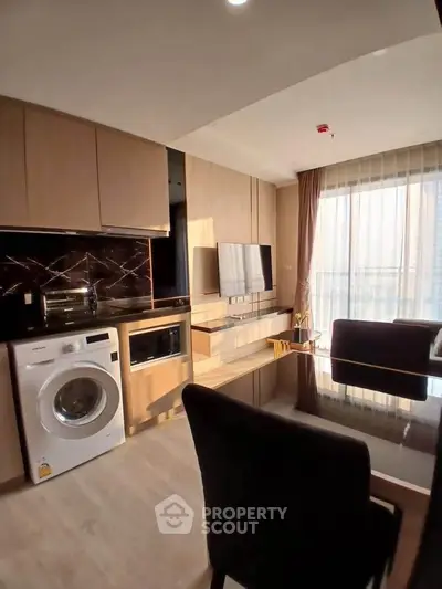 Modern apartment interior with washing machine and dining area, featuring sleek cabinetry and large windows.