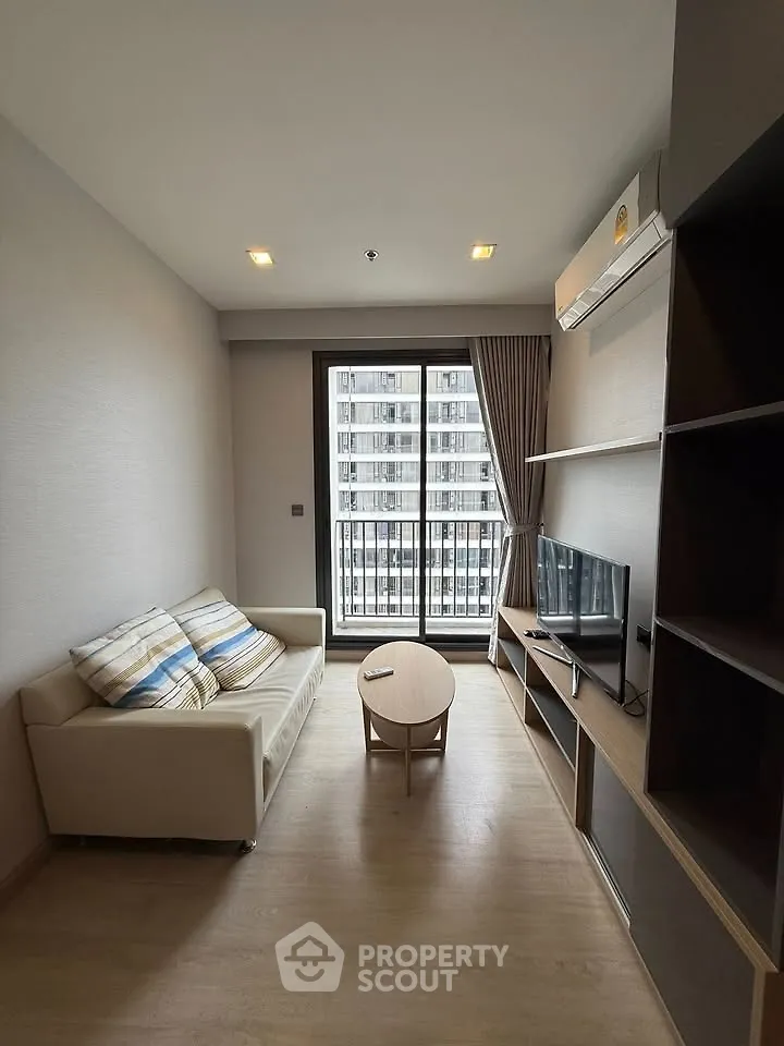 Modern living room with cozy sofa, TV, and large window in a high-rise apartment.
