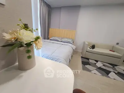 Cozy bedroom with modern decor, featuring a comfortable bed, stylish sofa, and elegant floral arrangement.
