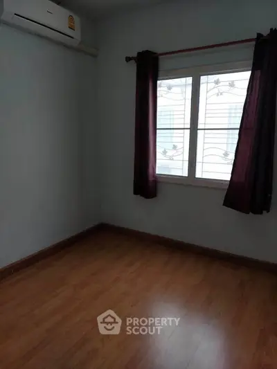 Spacious empty room with wooden flooring and large window, perfect for customization.