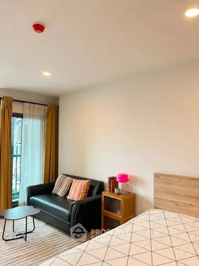 Cozy bedroom with modern decor, featuring a stylish sofa and natural light from large windows.