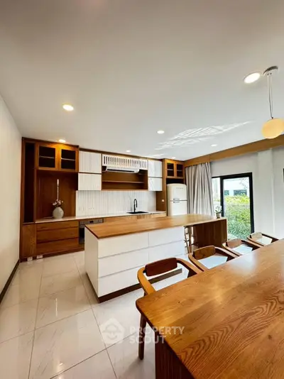Modern kitchen with wooden cabinets and island, featuring open layout and large windows.