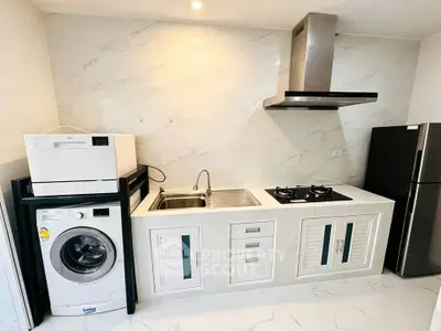 Modern kitchen with gas stove, washing machine, and sleek cabinetry in a stylish apartment.