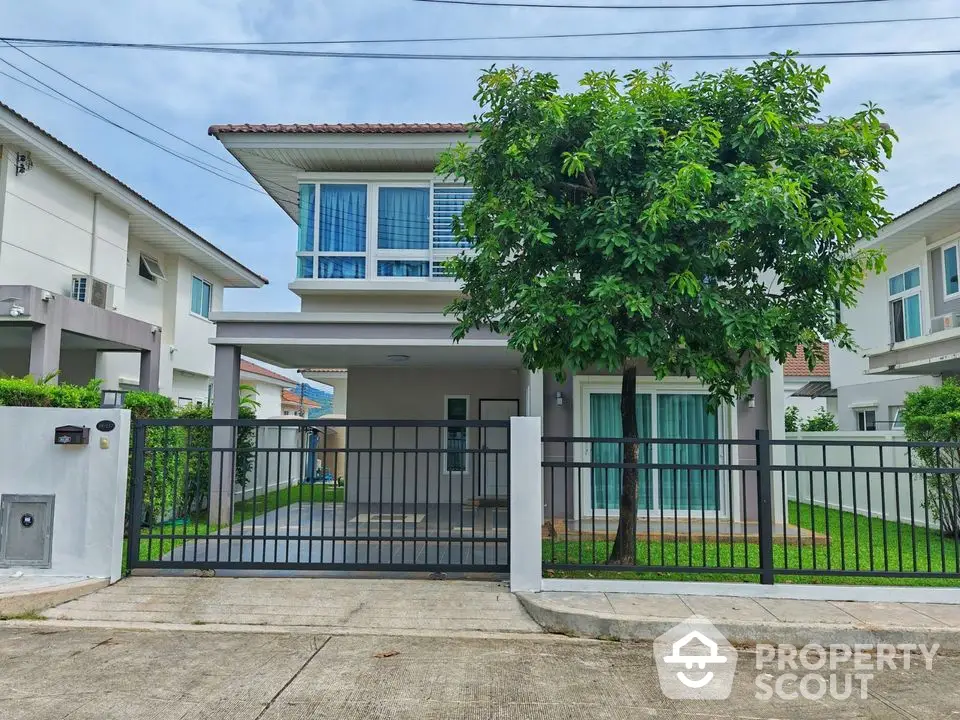 Modern two-story house with lush garden and gated entrance in suburban neighborhood.