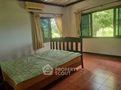 Spacious bedroom with large windows and serene garden view, featuring a cozy bed and air conditioning.