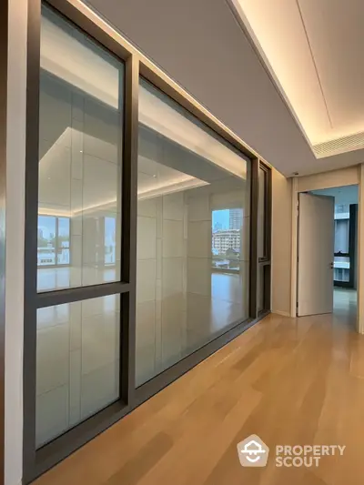 Spacious and modern living room with large windows offering ample natural light and a serene city view, featuring sleek wooden flooring and a contemporary design.