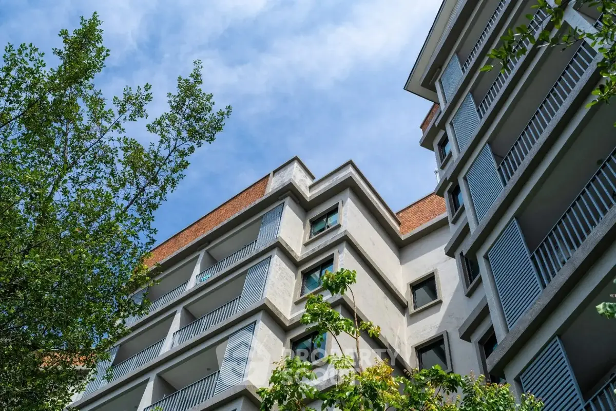 Modern apartment building exterior with lush greenery and blue sky backdrop.