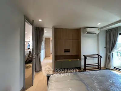 Spacious modern bedroom with wooden flooring and balcony access in a stylish apartment.