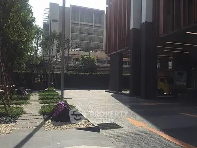 Modern building entrance with landscaped walkway and urban surroundings.