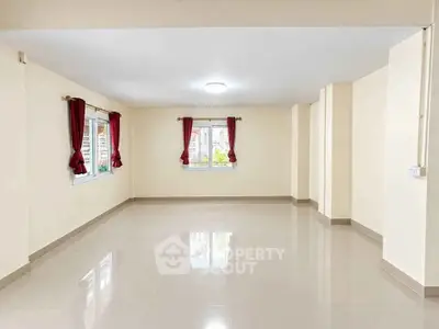 Spacious empty room with large windows and red curtains, perfect for customization.