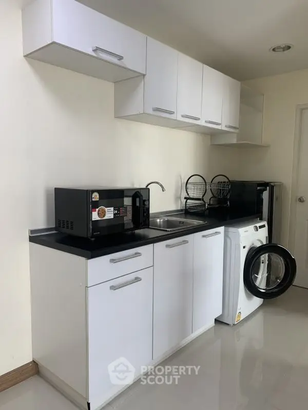 Modern kitchen with sleek white cabinets and appliances including washing machine and microwave.