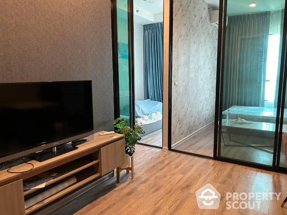 Modern apartment interior with wooden flooring and glass partition, featuring a cozy living area and bedroom.