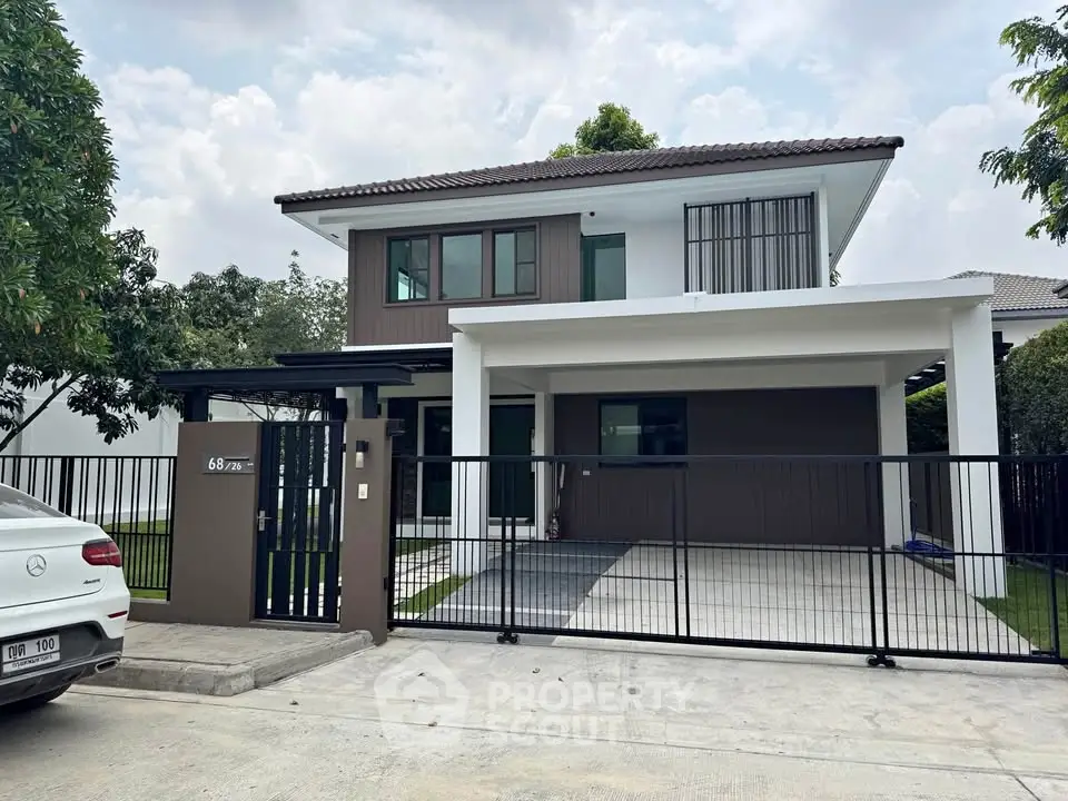 Modern two-story house with gated driveway and lush greenery, perfect for family living.