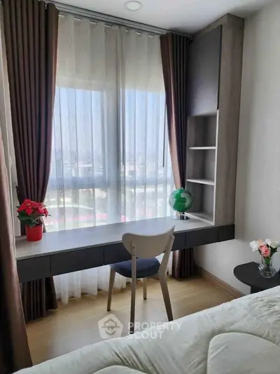 Cozy bedroom with study nook and large window offering natural light and city view.